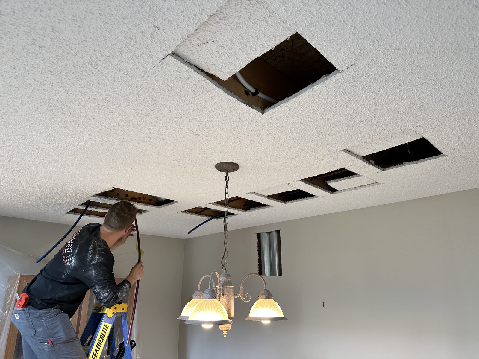 Crew member cutting a clean rectangular drywall access opening in a ceiling during a repipe