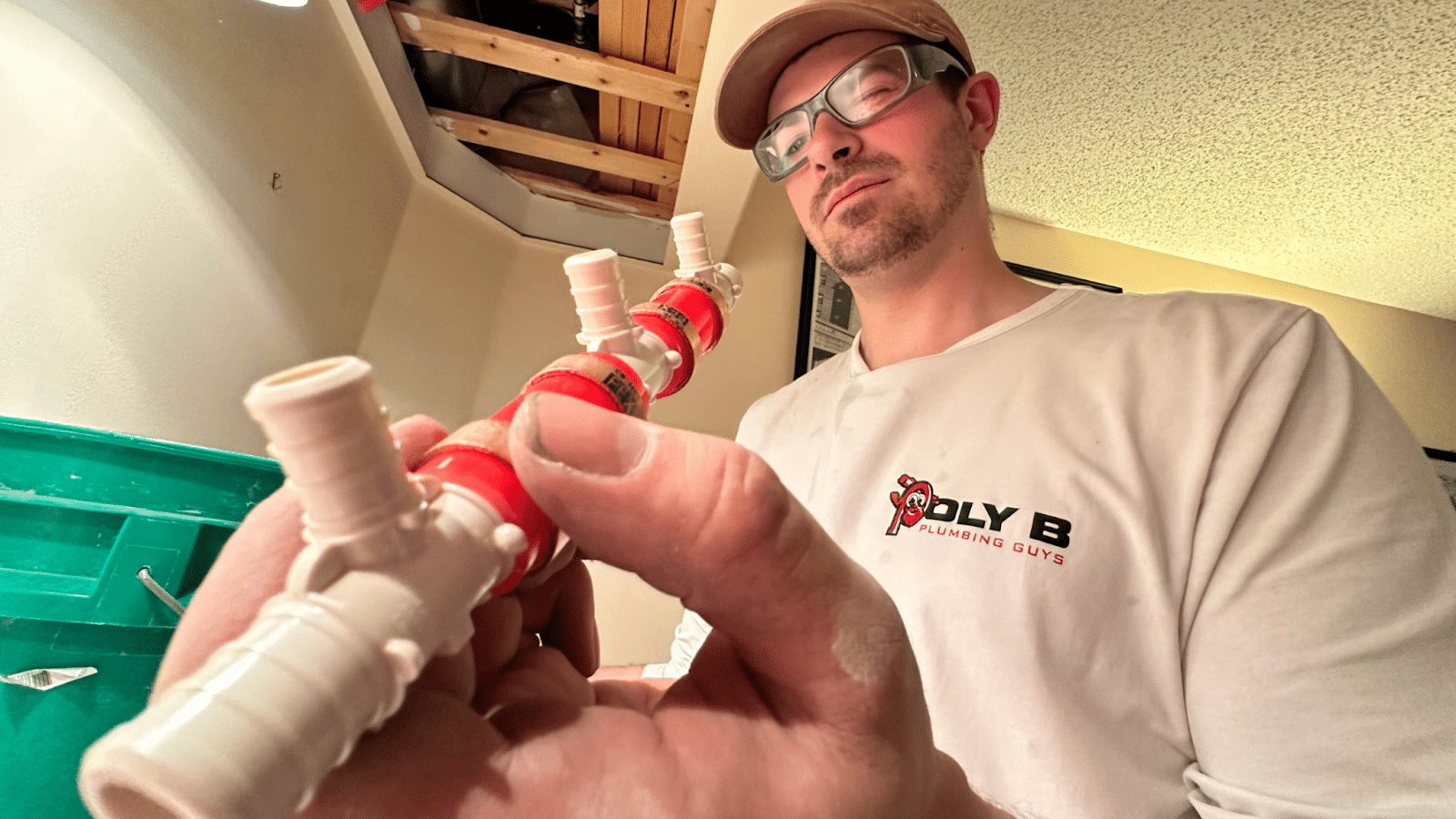 Plumber holding removed Poly B fittings, including a plastic insert tee and a crimped transition, cut out during a repipe