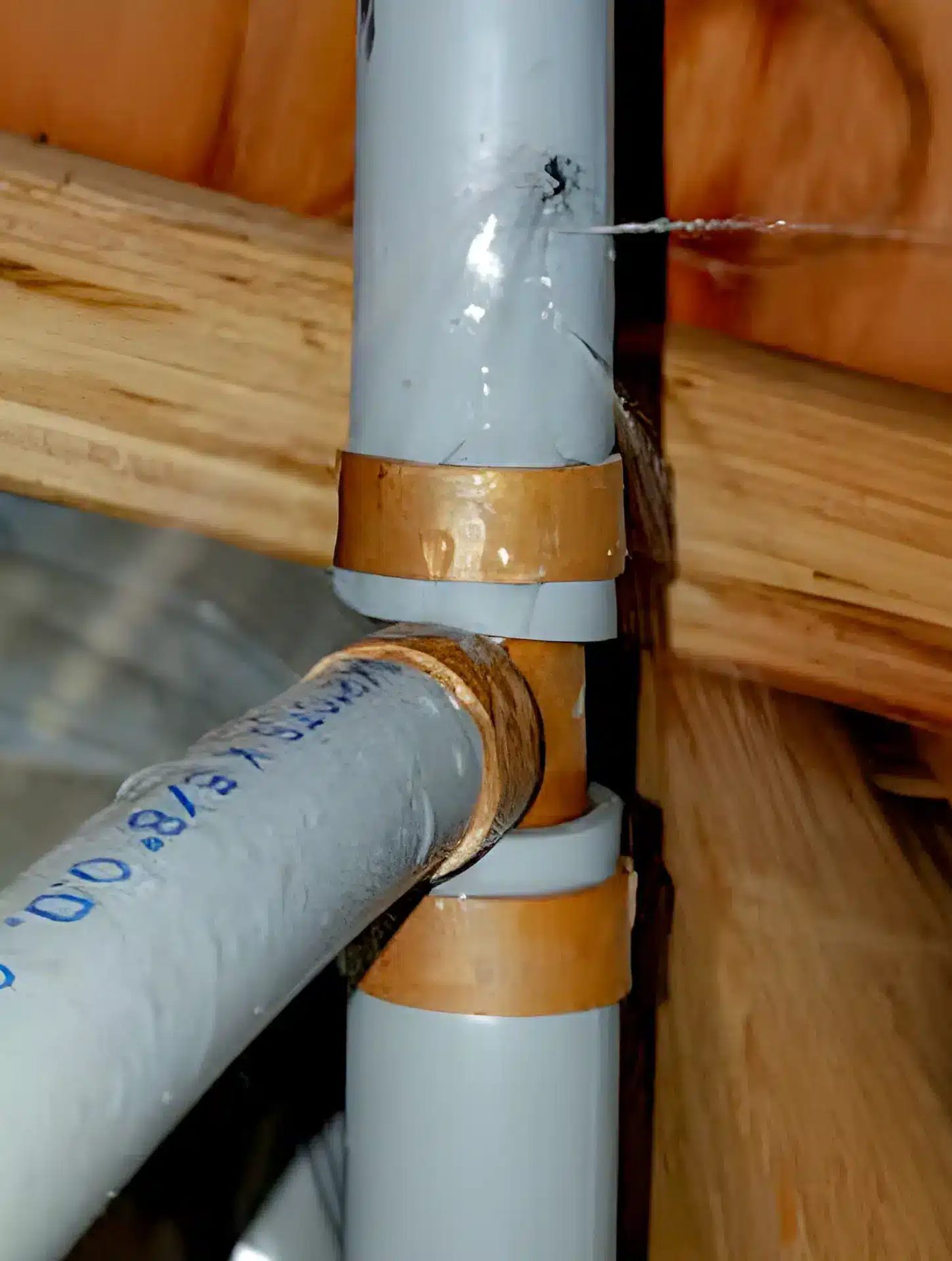 Grey Poly B pipe joined with copper crimp-ring fittings along a floor joist, the Canadian-style metal fitting installation