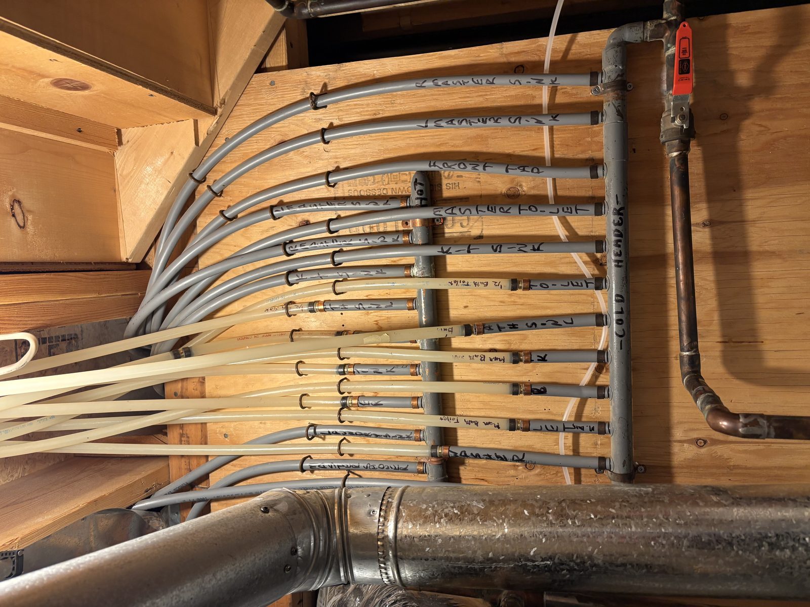 A full-home Poly B distribution manifold: more than a dozen grey flexible lines, each hand-labelled by room, fanning from copper crimp tees on a header