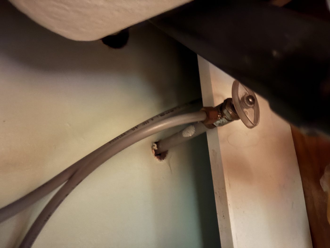 Grey flexible Poly B pipe under a sink, curving from the wall to a shutoff valve joined with a copper crimp fitting